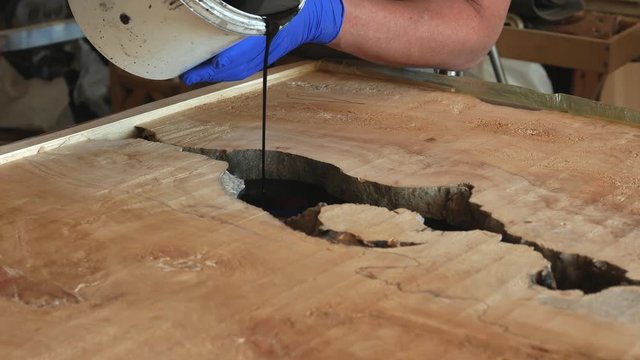 the carpenter, joiner, woodworker pours black epoxy resin from the maple top