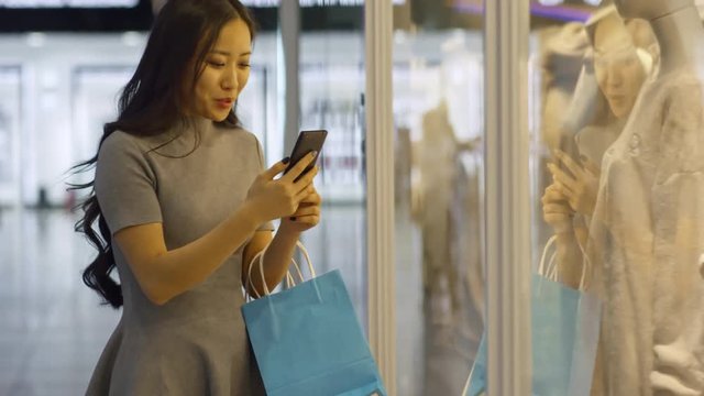 Medium shot of young Asian woman talking to friend via video call when shopping for clothes