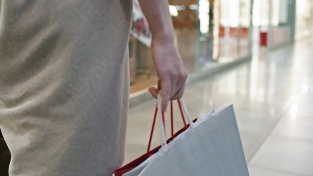 Close up shot of unrecognizable woman with paper bags walking along shopping mall hallway, rear view follow shot