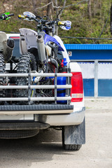 Rear viwe with two dirt bike motorcycles on the back of the truck with safety gear in residential...