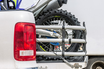Rear viwe with two dirt bike motorcycles on the back of the truck with safety gear in residential setting.