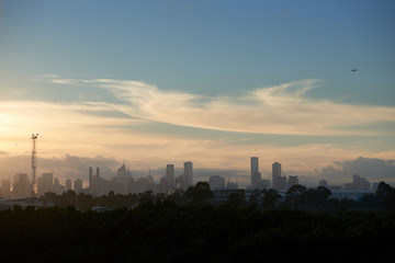 Melbourne city skyline in a hazy morning light with an airplane in the sky