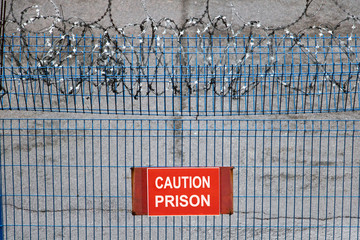 Iron fence with barbed wire. Metallic fence with red warning sign Caution Prison.