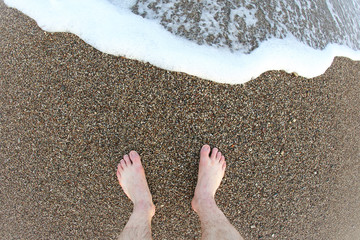 human feet on the sandy beach near the waves
