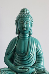 Head-on image of a jade colored Bhudda statue on a grayish-white background with light cast on one...