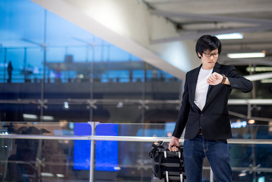 Young asian businessman checking the time from his watch while waiting for check-in in the international airport terminal, business travel concept