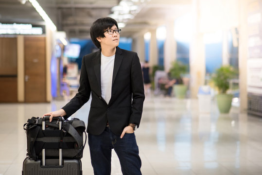 Young asian businessman with his suitcase luggage and backpack waiting for airline flight in the international airport terminal, man in business travel concept