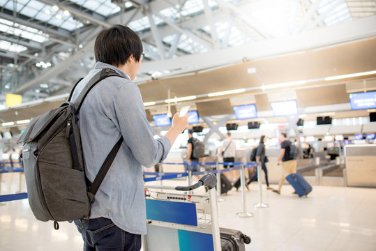 young asian check in online by using smartphone and waiting for drop his luggage at airline check-in counter inside the international airport terminal, travel lifestyle concept