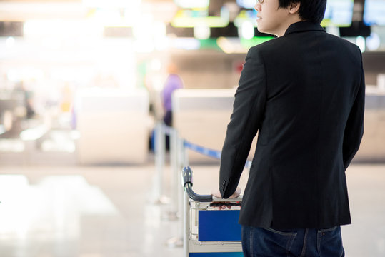 Young asian businessman with his luggage on airport trolley waiting for check in at airline counter in the international airport terminal, business travel concept