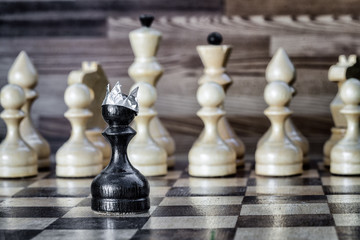 Passing pawn on the chessboard. Black pawn in the crown against a row of white figures. Business success concept.