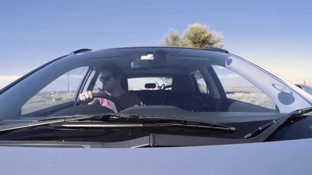 Man in Pink Shirt Driving Sedan through Dry Barren Landscale