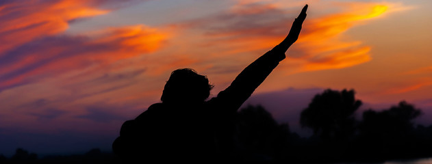 Panorama of silhouette of a man at sunset with his hands up. Concept of victory