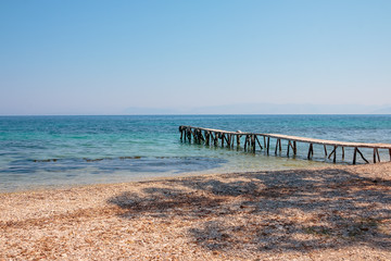 Fototapeta na wymiar Wooden pier turquoise sea water sunny day, stones beach, greece island. Romantic wild place. Clear water sea. wooden pier goes to the sea, Sunny weather, the horizon line.Copy space