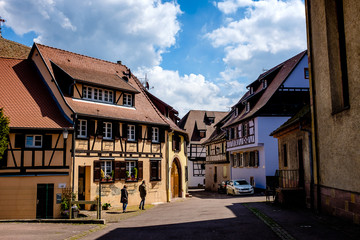 Naklejka premium people walking along cobbled street between beautiful half-timbered houses in Eguisheim, Alsace