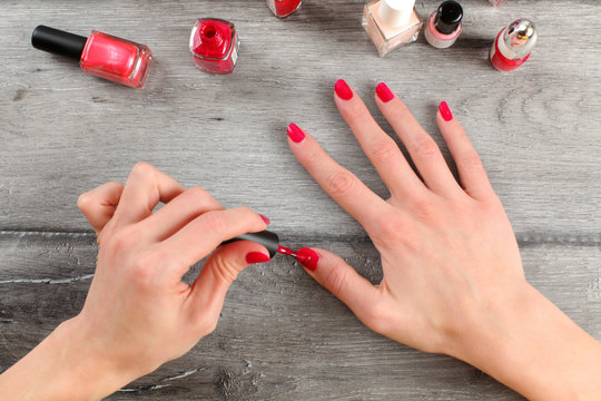 Table top view on young woman hands, applying second coat of red nail polish,  with more bottles of nail varnish in background placed on gray wood desk.  Stock Photo | Adobe Stock