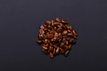 A handful of pine nuts in shells on black background Three hole cedar cones Copy space Top view