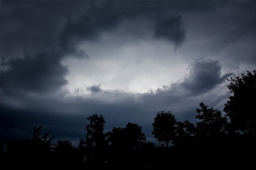 Dark dramatic dark sky and black silhouettes of trees. Stormy weather on summer day_