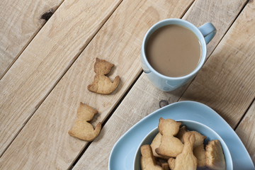 Delicious gingerbread cooked on a blue plate, a cup of coffee from milk to a light wooden background.