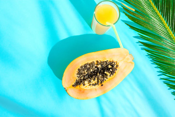 Flat Lay Composition Tall Glass with Fresh Tropical Fruit Juice Halved Papaya Palm Leaf on Blue Background. Harsh Midday Light Sunlight Leaks. Summer Seaside Vacation Fashion Concept. Swimming Pool