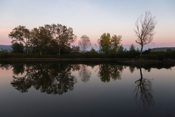 Fototapeta na wymiar A symmetric photo of a lake, with trees and clouds reflections o