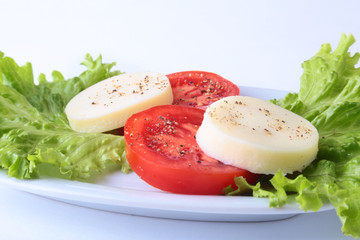 Portion of Mozzarella with Tomatoes, lettuce leaf and Balsamic dressing on white plate. selective focus close-up shot.