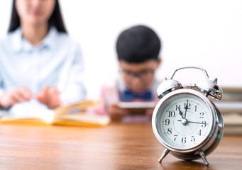 Selective focus photo at clock, school boy using mobile phone playing game, don’t interest homework