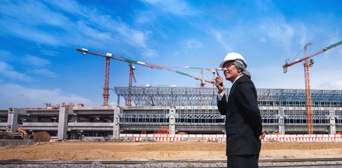 Asian business man with Walky Talky on construction site and tower cranes in background