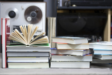 Open book, stack of hardback books on table. Top view.