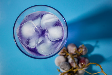 cocktail with grape on blue background top view.