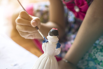 Close up hand of little girl painting plaster doll with blue water color, practice art concept.