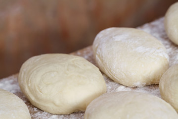 Raw homemade pies. Uncooked patties from yeast dough with stuffing are lying on a wooden plank and ready for baking. Closeup, selective focus, brick background