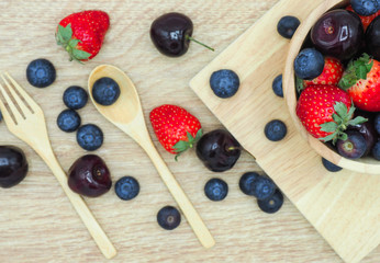 Fresh summer fruits, Cherry, strawberry and blueberry in wooden bowl isolated on wood background.