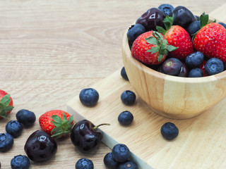Fresh summer fruits, Cherry, strawberry and blueberry in wooden bowl isolated on wood background.