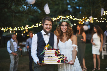 Bride and groom holding a cake at wedding reception outside in the backyard.