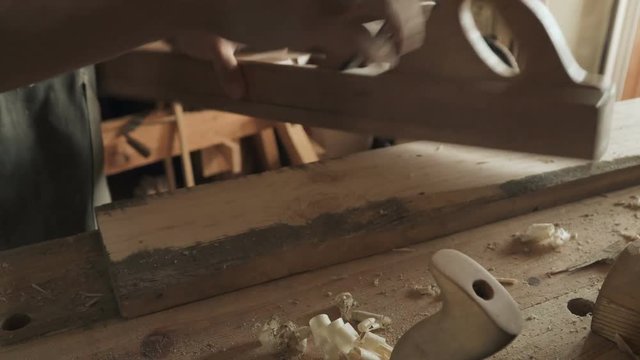 Skilled craftsman carpenter whittles workpiece of wooden board with jack-plane in a workshop. Making handmade furniture.