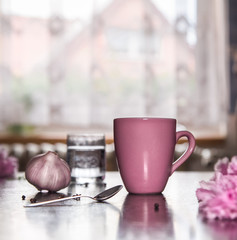 Pink cup, pink flowers.Garlic bulb.Window morning light. House, as background.