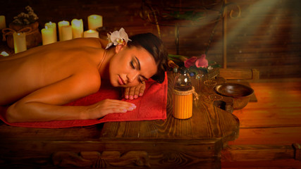 Massage of woman in spa salon. Girl on candles background in therapy room. Luxary interior in oriental therapy salon. Sun rays flare for female have relax after sport. Morning light from right.