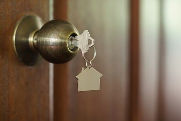 Home key with house keychain in keyhole, property concept