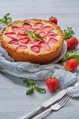 Just baked homemade strawberry cheesecake on the gray background decorated with fresh strawberries, mint leaf, gray cloth, vintage silver knife and fork. Delicious summer dessert. Side view