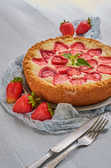 Homemade strawberry cheesecake on the gray background decorated with fresh strawberries, mint leaf, gray cloth, vintage silver knife and fork. Delicious summer dessert. Close up view