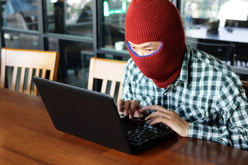 Masked hacker wearing a balaclava stealing information data with laptop. Internet crime concept.