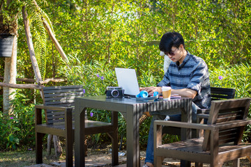 Fototapeta premium Young man wearing glasses sitting using a laptop in a garden