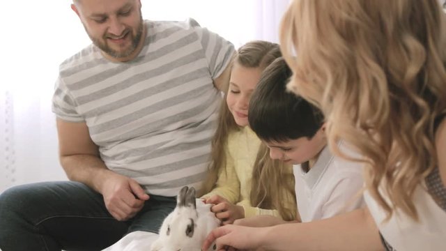Portrait of happy family that is stroking a rabbit while sitting on the sofa