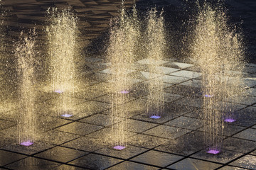 Fountain splashes on dark background with color lights on bottom