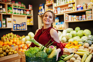 Girl in red holding different vegetables on fruits store.