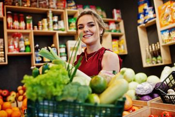 Girl in red holding different vegetables on fruits store.
