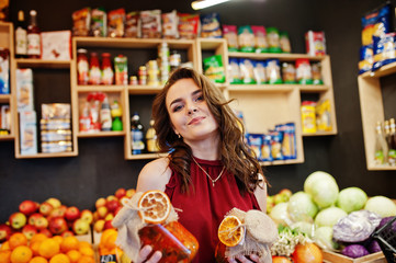 Girl in red holding jam in a jar on fruits store.