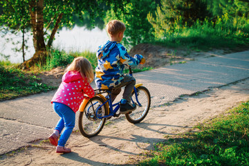 little girl push little boy on bike in nature