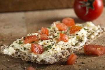 Crispbread with melted cheese and pieces of cherry tomatoes seasoned with ground black pepper