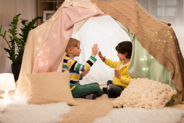 childhood, hygge and friendship concept - happy boys playing clapping game in kids tent or teepee at home